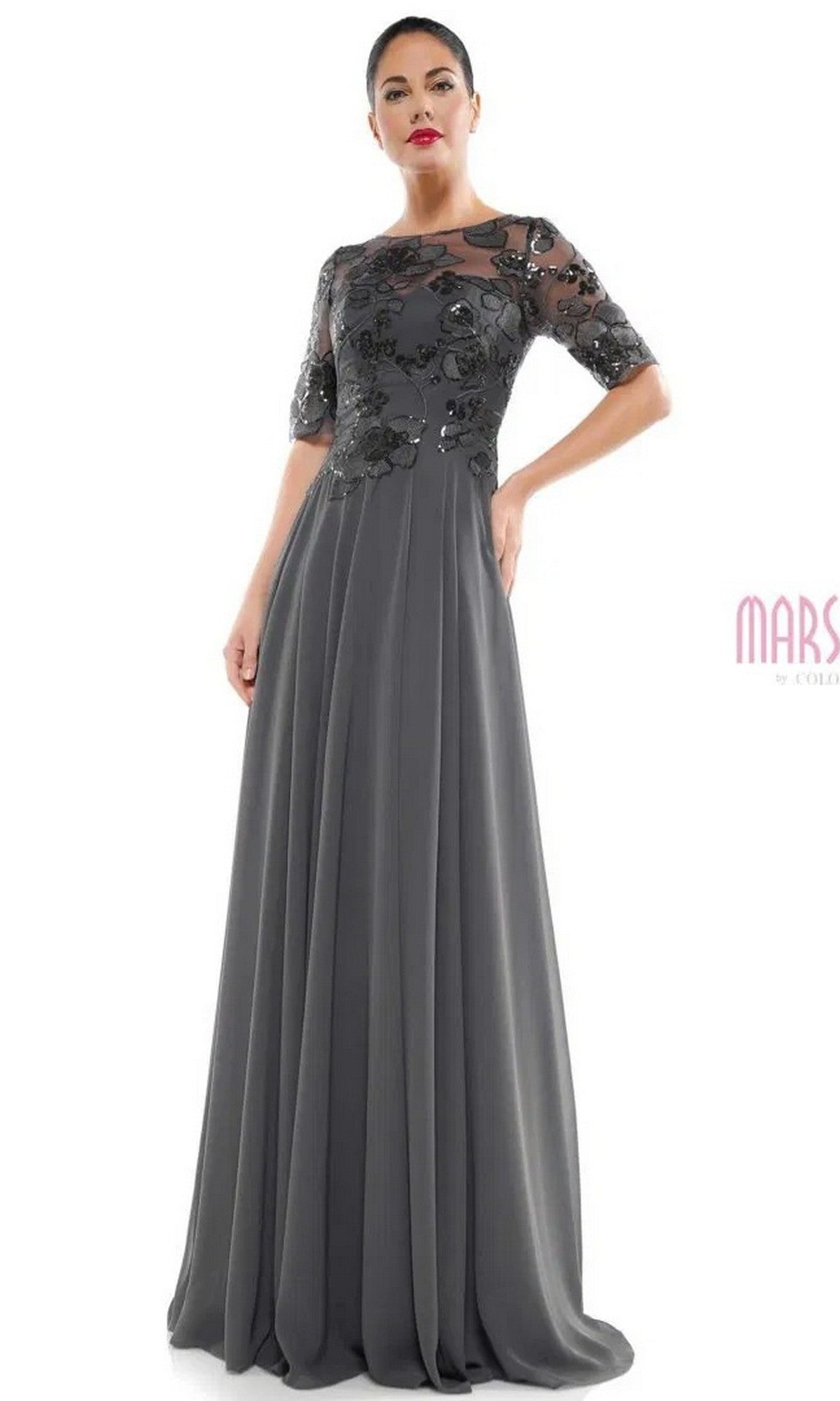 A woman models the Marsoni M286 long formal dress in charcoal grey, featuring sheer short sleeves and floral embroidery on the bodice, set against a plain white background.